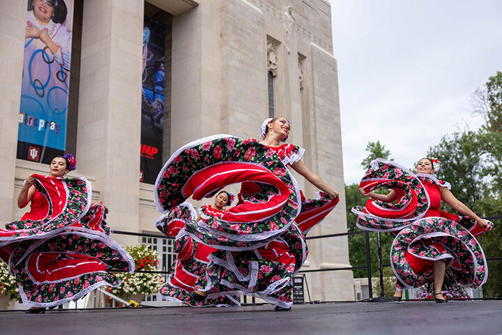 Women dancers wearing traditional hispanic dresses perform outdoors.